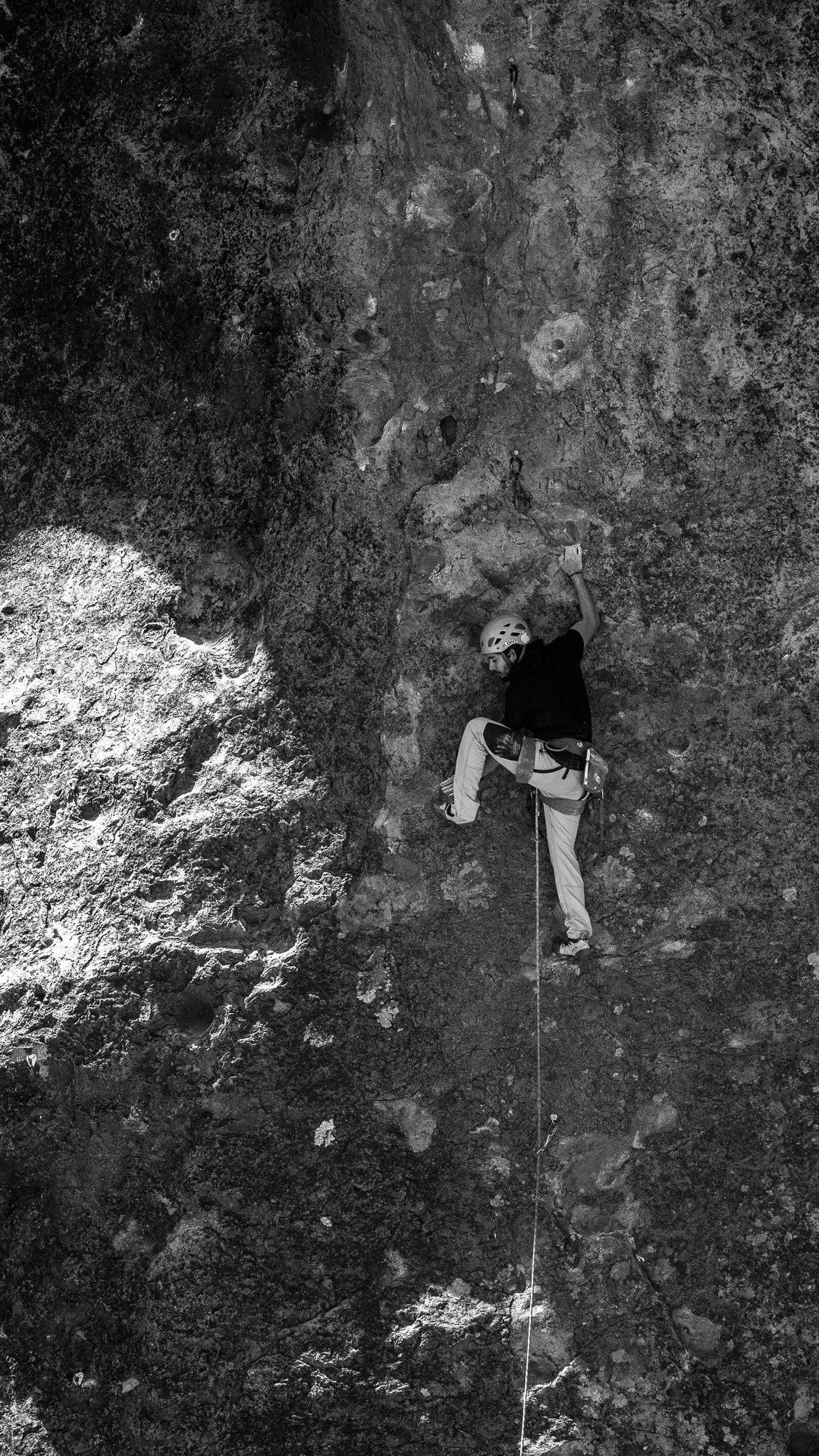 A person wearing climbing gear and a helmet provided by wildkoala is rock climbing on a vertical outdoor wall, using hand and foot holds.