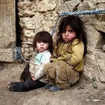 Two young children sitting against a rough stone wall, with a dark animal curled up on the ground in front of them.