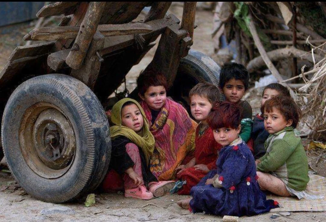Group of children sitting and hiding under a wooden cart in a dusty, debris-filled environment.