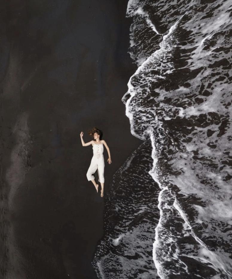 A person in a black swimsuit lying on a large rock formation among rocky terrain. Captured by Ines Prelovsek in Nosara, Costa Rica. 