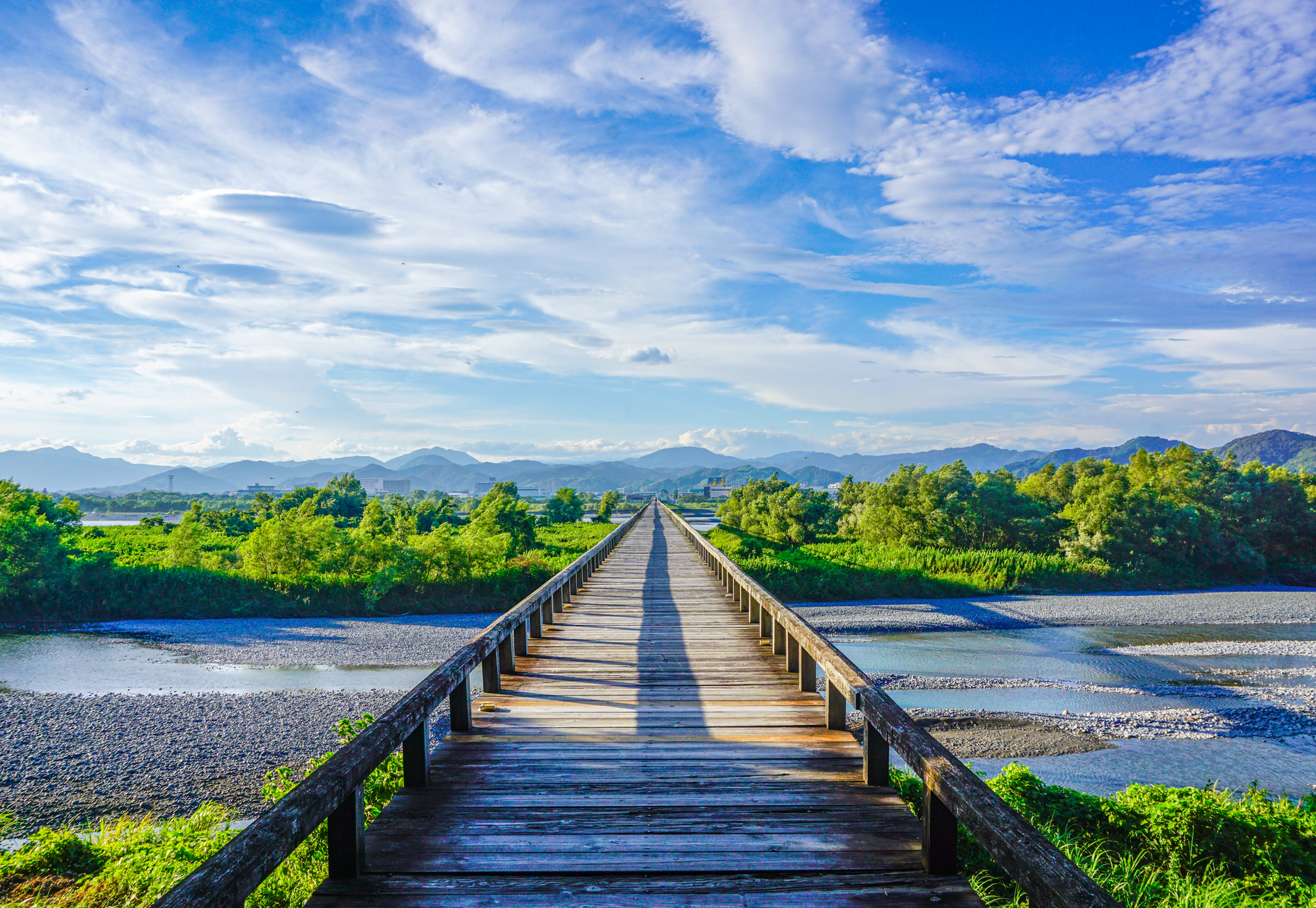 Horai Bridge, the world's longest wooden pedestrian bridge, stretches across the Oi River in Shimada, Shizuoka, under a clear blue sky.