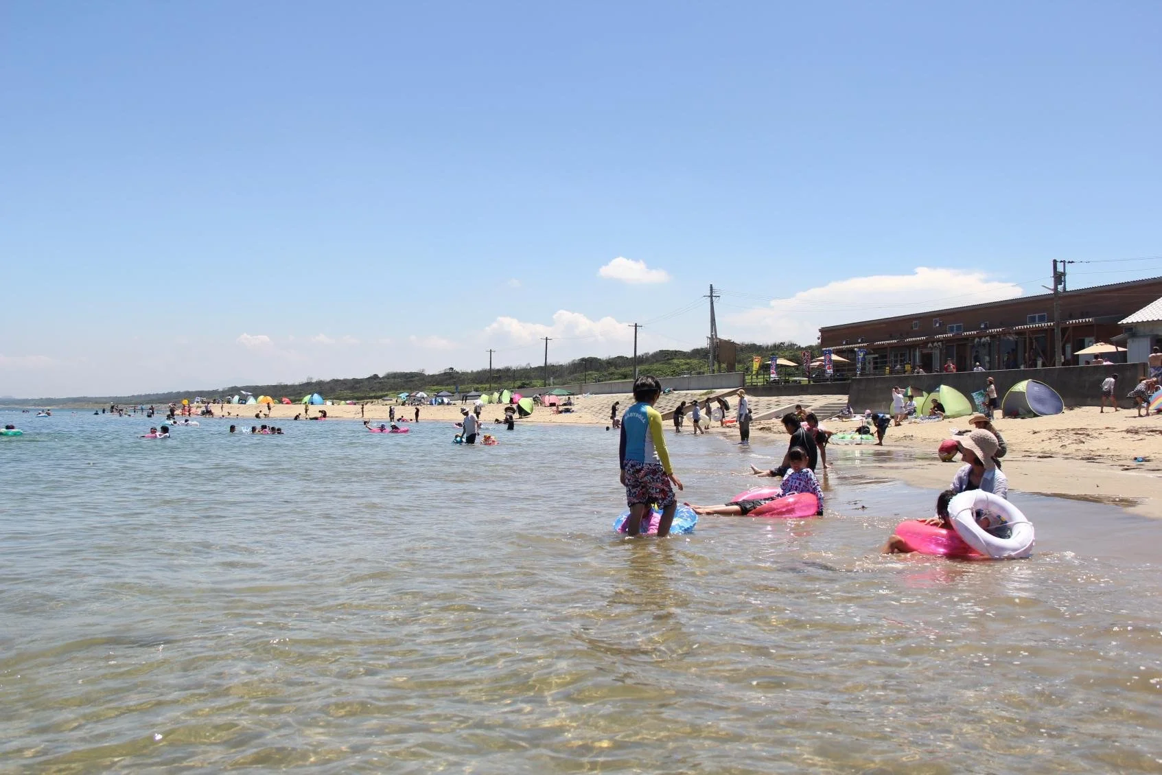 Families relaxing on pink inflatable rings in the shallow calm waters of Hatsu Beach, a white-sand family-friendly coast in Okagaki, Fukuoka.