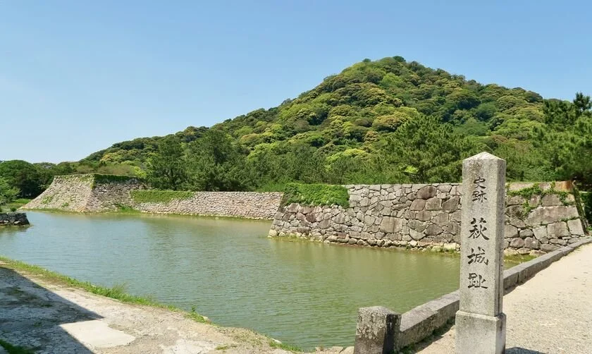 Stone moat and inscribed pillar at the Ruins of Hagi Castle, framed by Mount Shizuki under a clear blue sky — a timeless samurai retreat in western Japan.