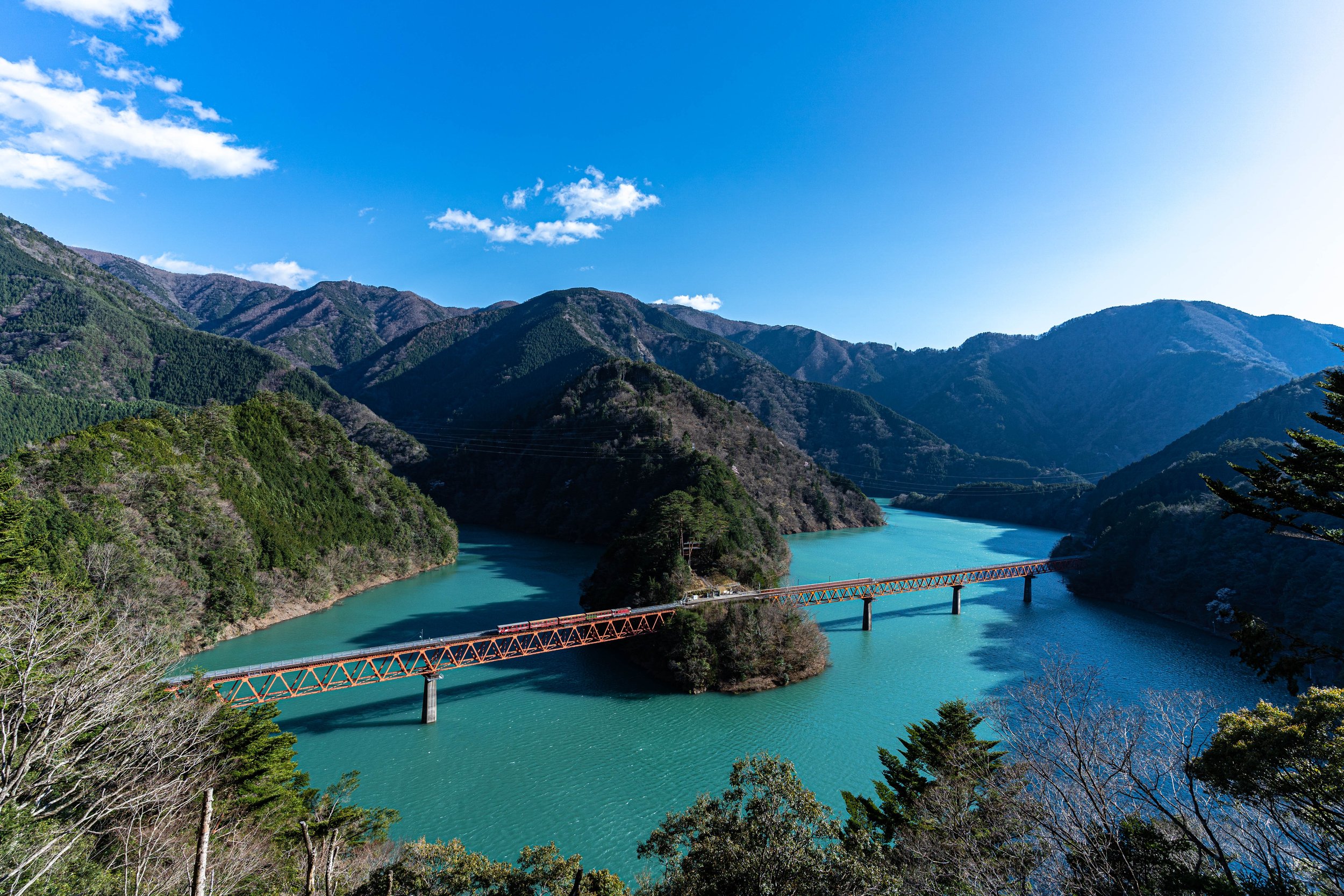 Red railway bridge over turquoise Lake Sessō in autumn — Oku-Oi Kozyo Station, a hidden gem in Shizuoka's mountains.