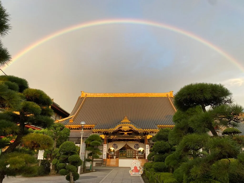Sano Yakuyoke Daishi temple in Tochigi, Japan, with a rainbow arching over its historic tiled roof at golden hour.