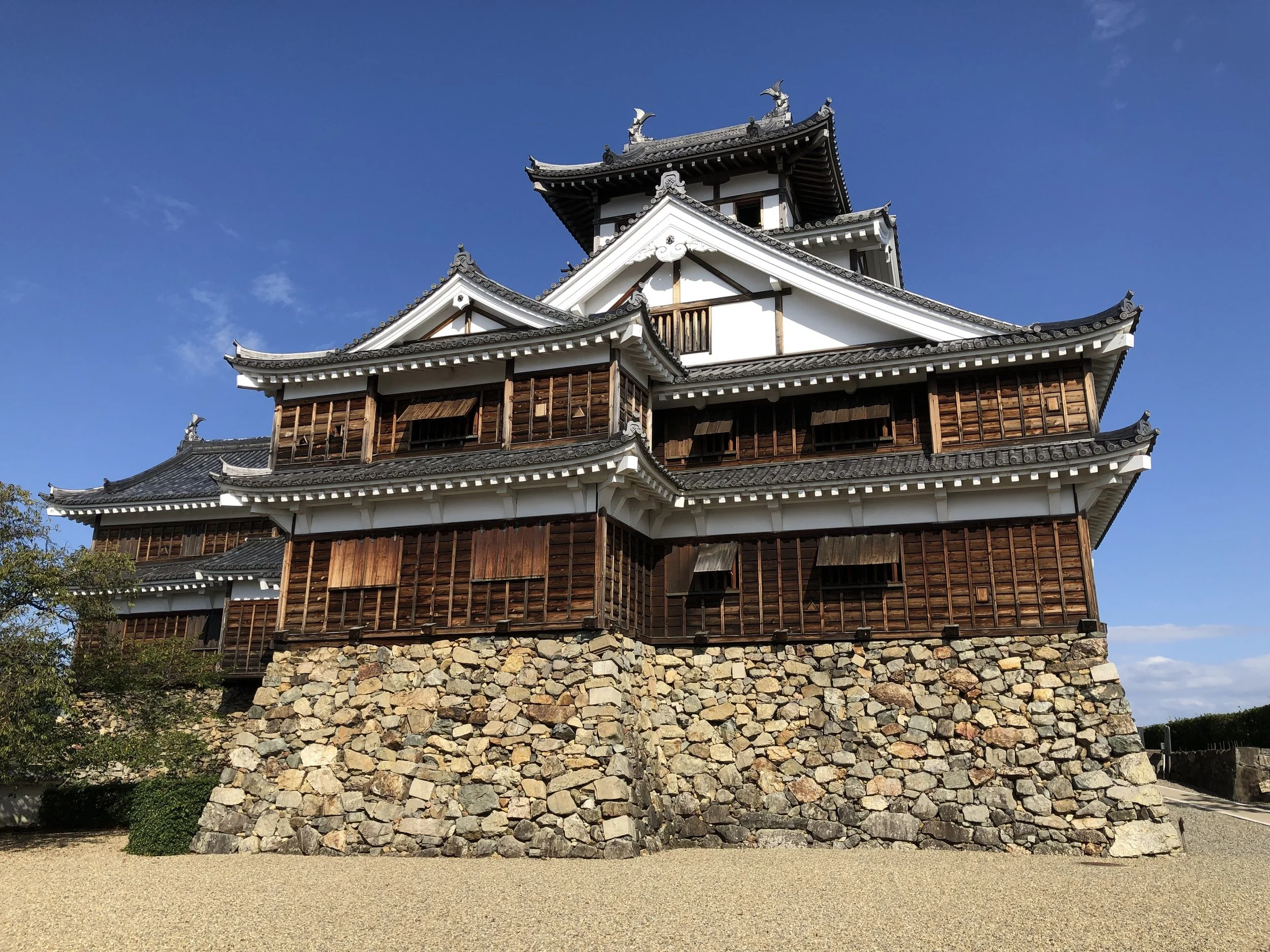 Fukuchiyama Castle keep rising over original stone ramparts under a clear blue sky — a hidden feudal gem in Kyoto Prefecture.