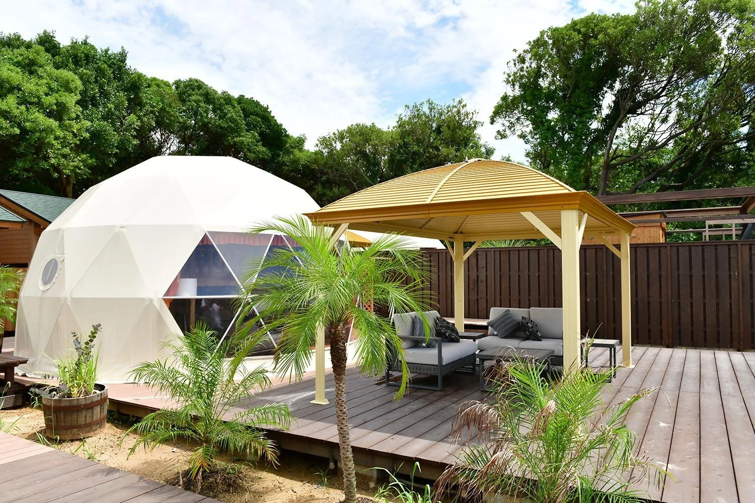 Dome tent and wooden gazebo lounge on a palm-lined deck at Jomon no Oka Glamping Resort in Ashiya Town, Fukuoka — a hilltop retreat above the Genkai Sea.
