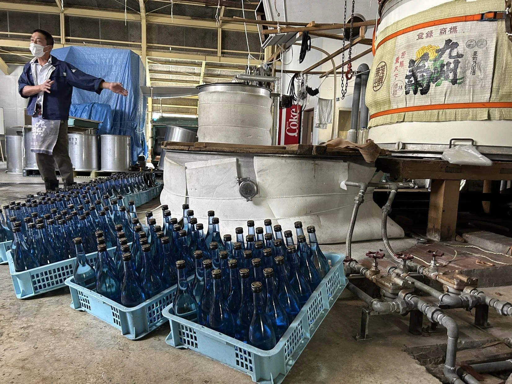 Interior of Hayashi Ryuhei Sake Brewery in Fukuoka — blue glass bottles in crates beside white fermentation tanks, where sake has been brewed since 1837.