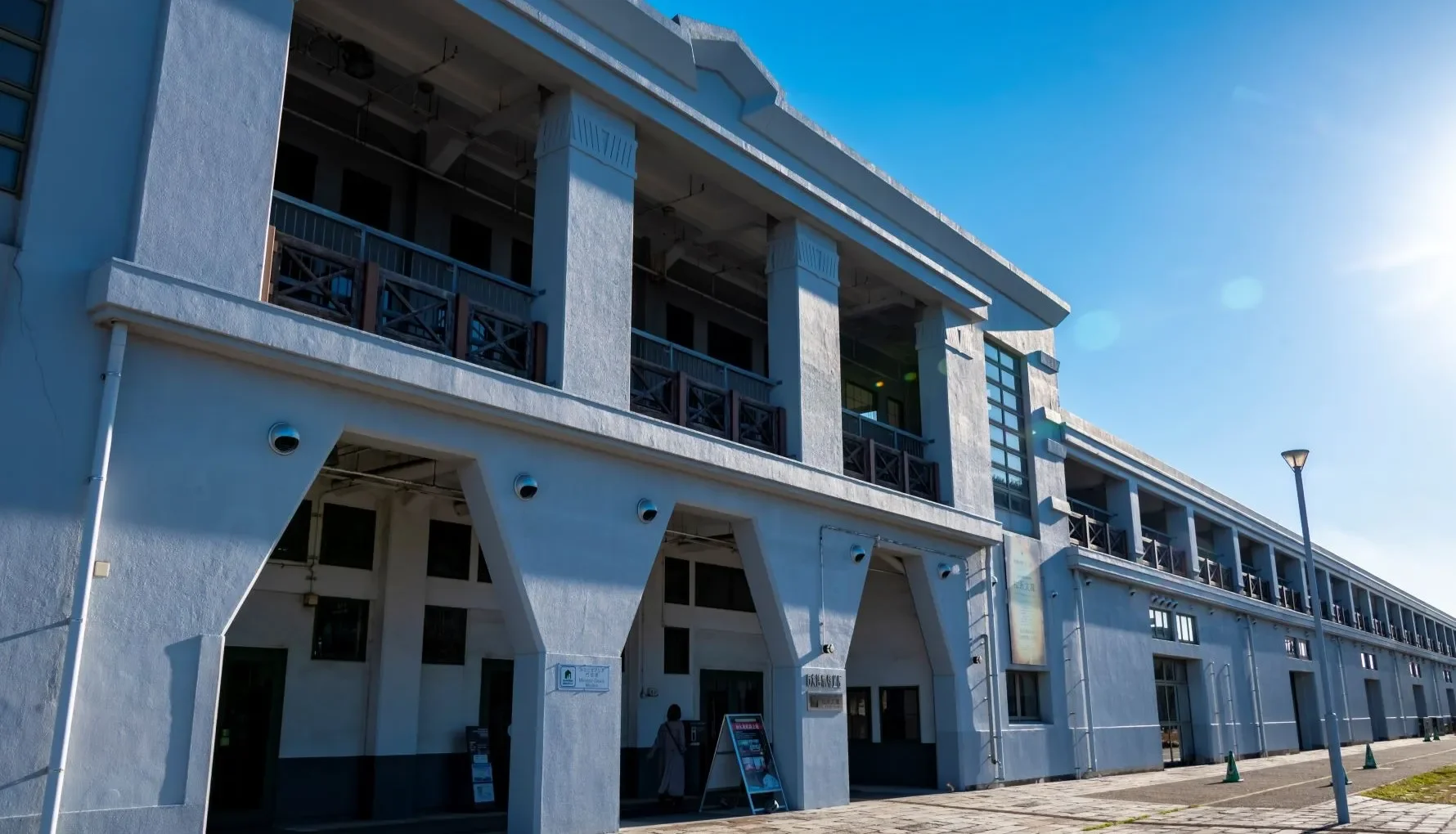 A modern building with glass doors and windows, decorated with flags and signs, including a cartoon tiger mascot wearing a white hat and cape, outdoors on a sunny day with trees in the background.