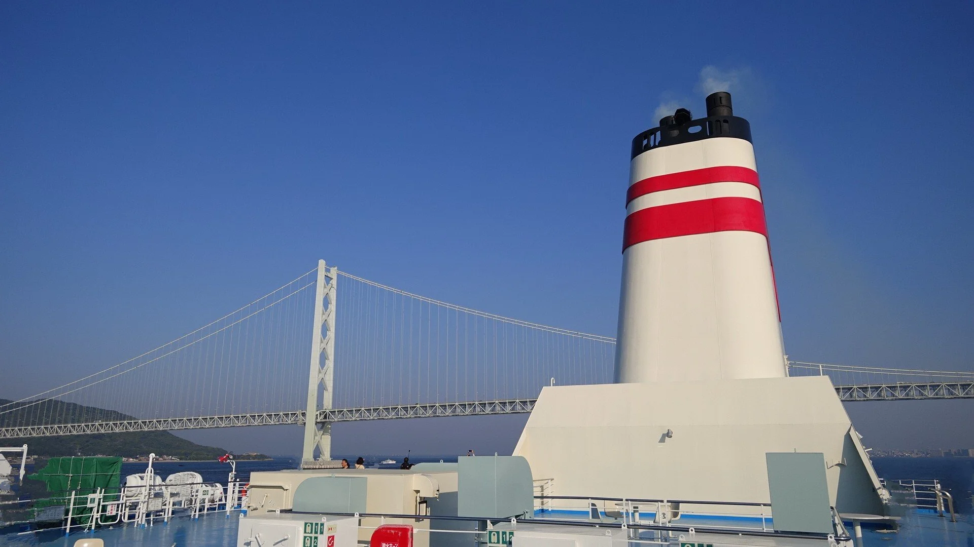 Hankyu Ferry smokestack framed against the Akashi Kaikyō Bridge at dawn — a rare slow-travel passage across Japan's Inland Sea.