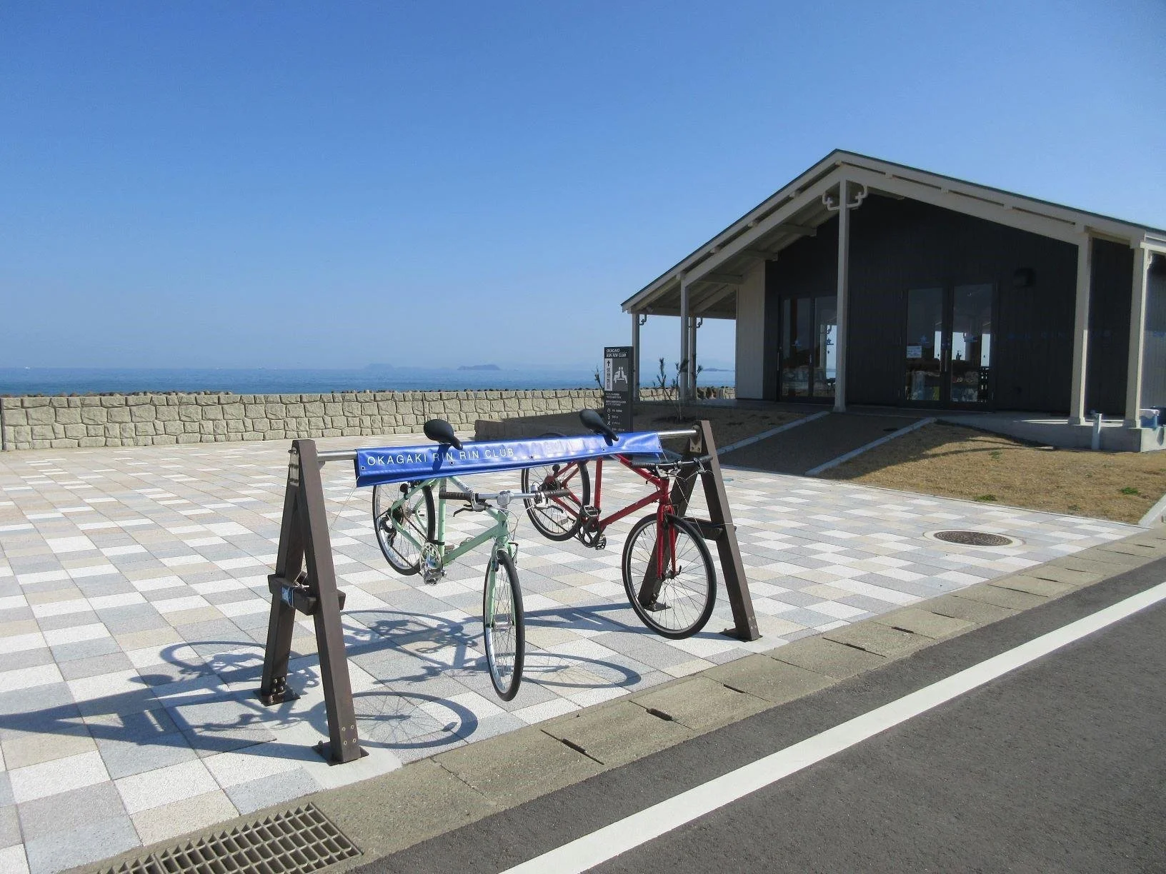 Colorful bicycles parked at Rinrin Club Okagaki, a seaside cyclist rest stop on Fukuoka's Hatsu Coast under a clear blue sky.