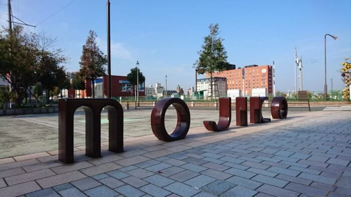 A bowl of udon noodle soup topped with green onions, tempura, beef, and a fish cake, served alongside onigiri rice balls wrapped in seaweed.