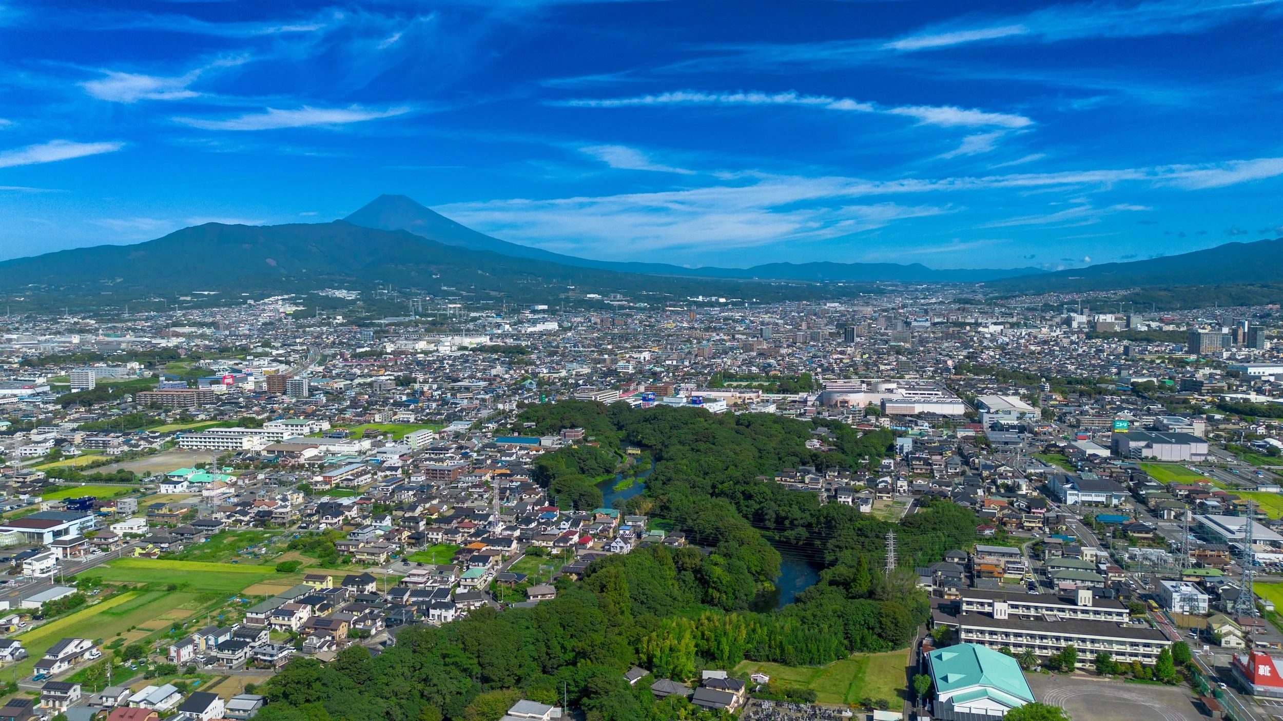 Aerial view of Kakita River Park and Shimizu Town with Mount Fuji rising beyond — a hidden gem of crystal-clear spring water in Shizuoka, Japan.