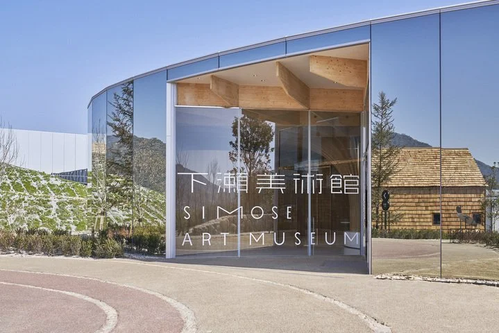 Simose Art Museum's mirrored glass facade reflecting green hills and blue sky in Otake, Hiroshima — a UNESCO-honored architectural gem.