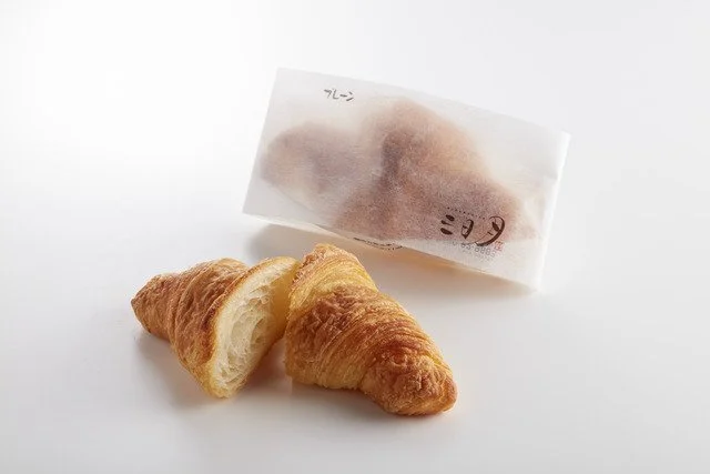 Two croissants and a wrapped pastry on a white surface.