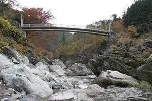 Sanbasekikyo Gorge in Fujioka, Gunma — a pedestrian bridge over the Kanna River framed by giant Sanbaseki rocks and autumn-colored hills.