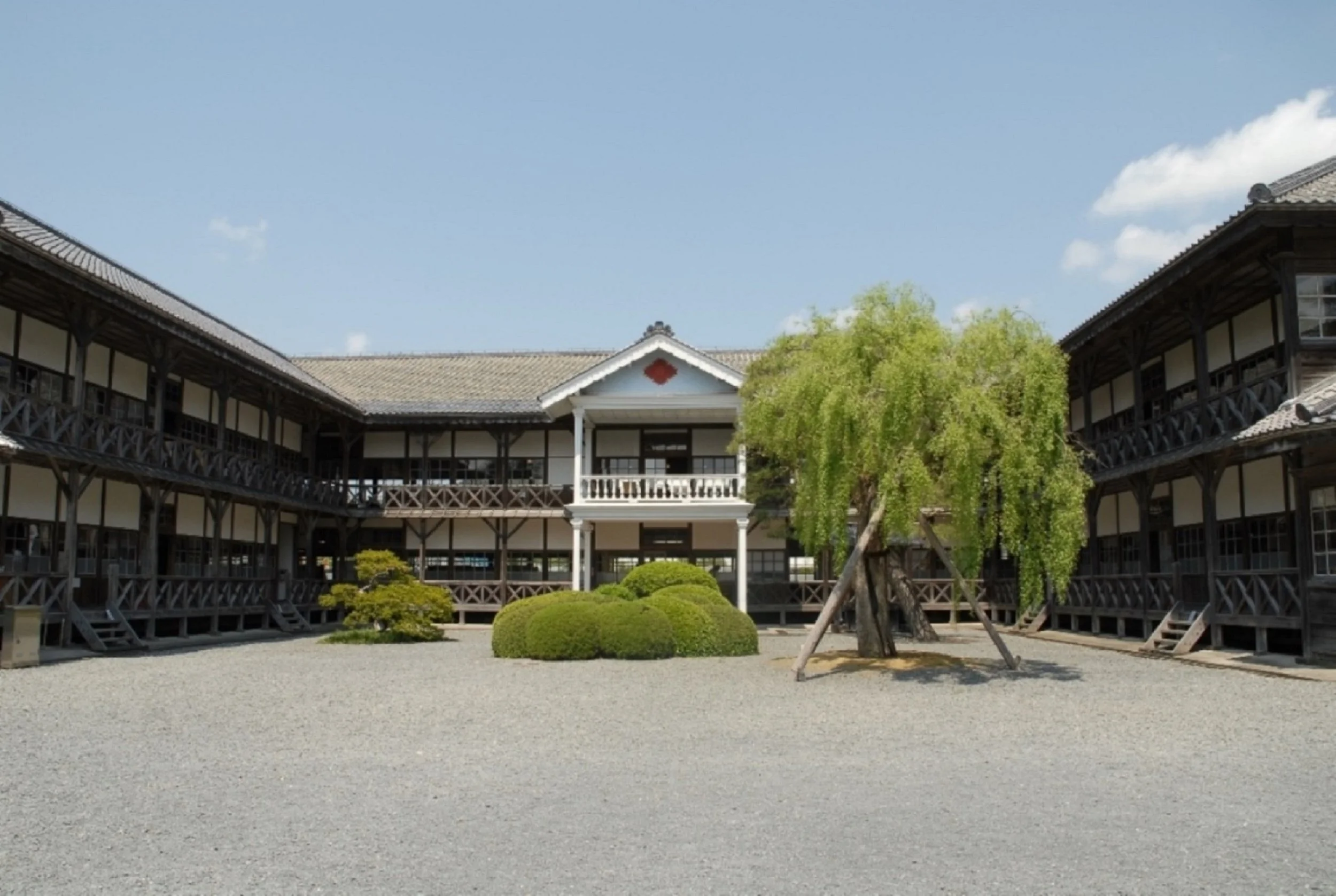 A U-shaped Meiji-era wooden schoolhouse with white walls and dark timber framing, set beneath a clear blue sky in Toyoma Town, Miyagi — a hidden gem of historical Japan.