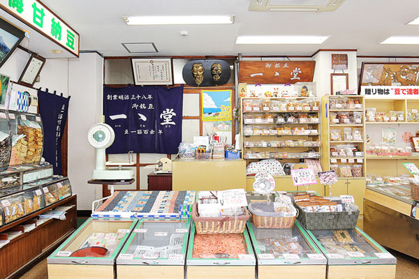 A bowl of udon noodle soup topped with green onions, tempura, beef, and a fish cake, served alongside onigiri rice balls wrapped in seaweed.