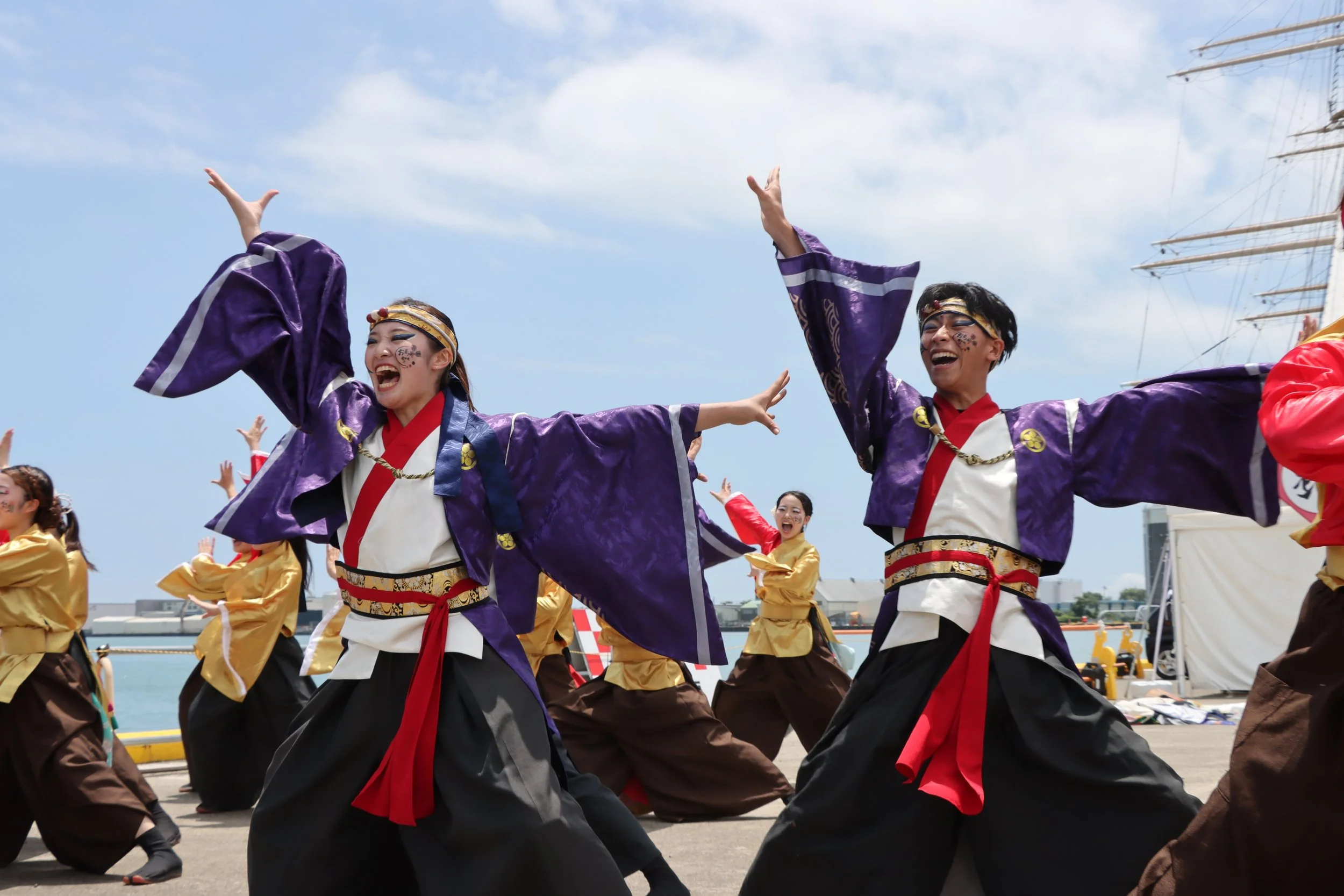 Performers in purple and gold costumes dancing at Odorakkasai festival by Yaizu harbor — a vibrant local summer celebration.