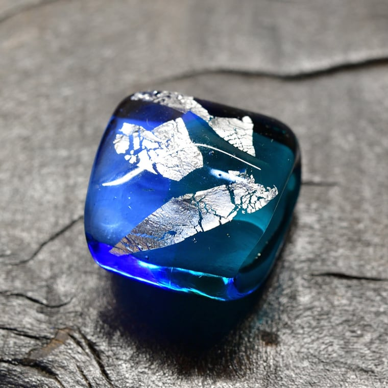 A dessert served in a tall glass with various toppings like fruit, beans, and cookies, viewed on a tray with a blurred background.