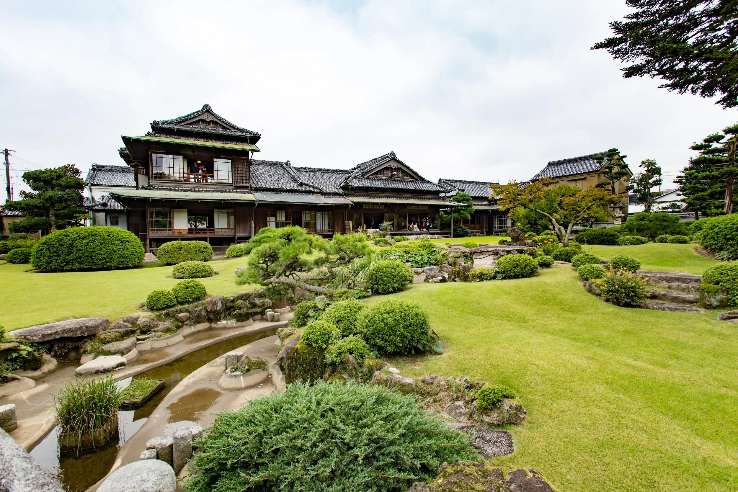 Former Ito Den-emon Residence in Iizuka, Fukuoka — traditional wooden mansion with tiled roofs overlooking a strolling garden with pond, pine, and stone arrangements.