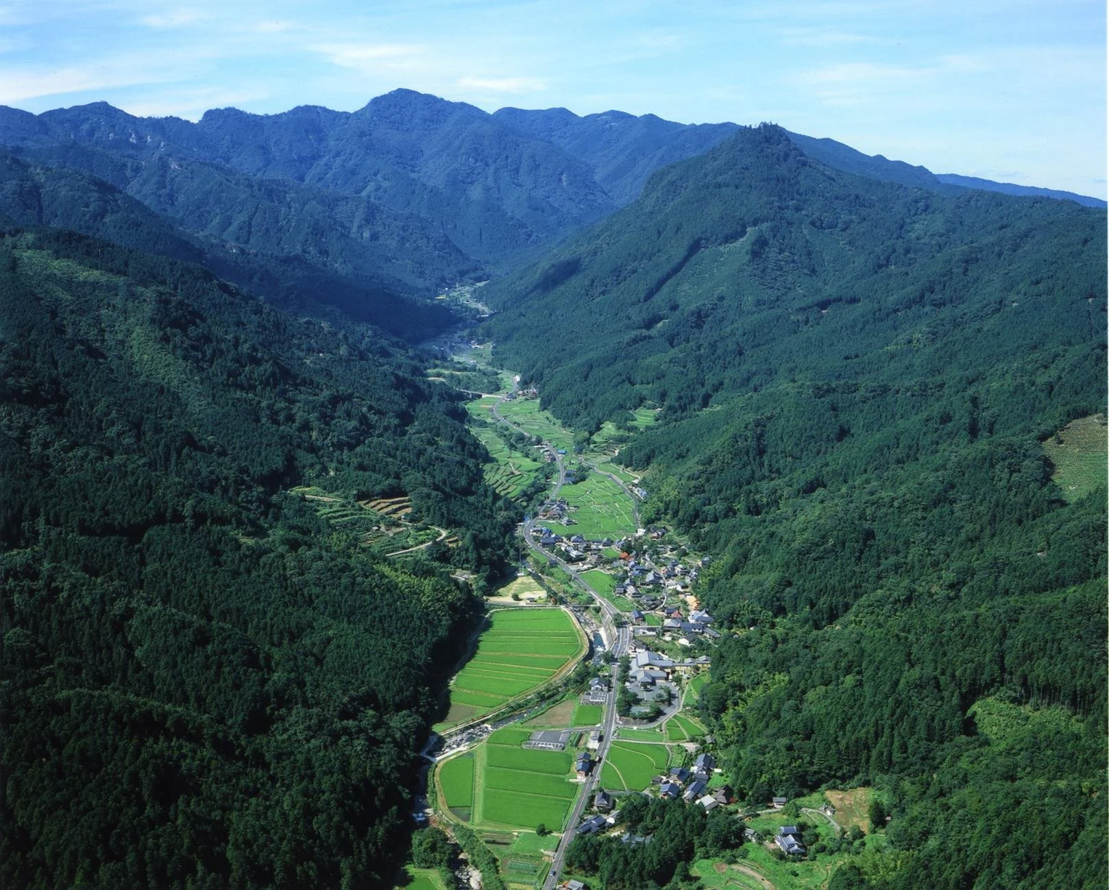 Aerial view of Mount Kubote's sacred valley in Buzen, Fukuoka — terraced green fields and a quiet mountain village surrounded by forested peaks.