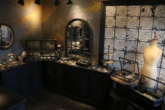 Interior of a boutique jewelry store with display cases, a dress form, and vintage decor.