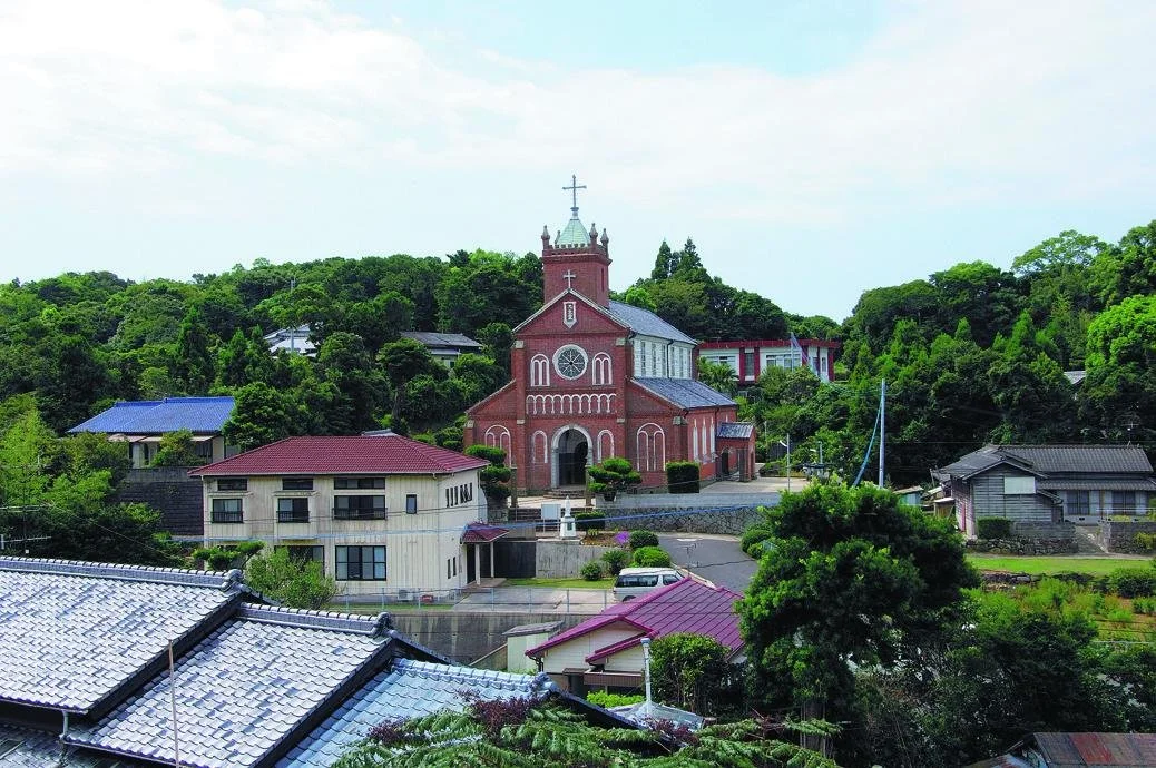 Red-brick Kuroshima Catholic Church rising above traditional tiled rooftops and forested hills on Kuroshima island, Nagasaki.