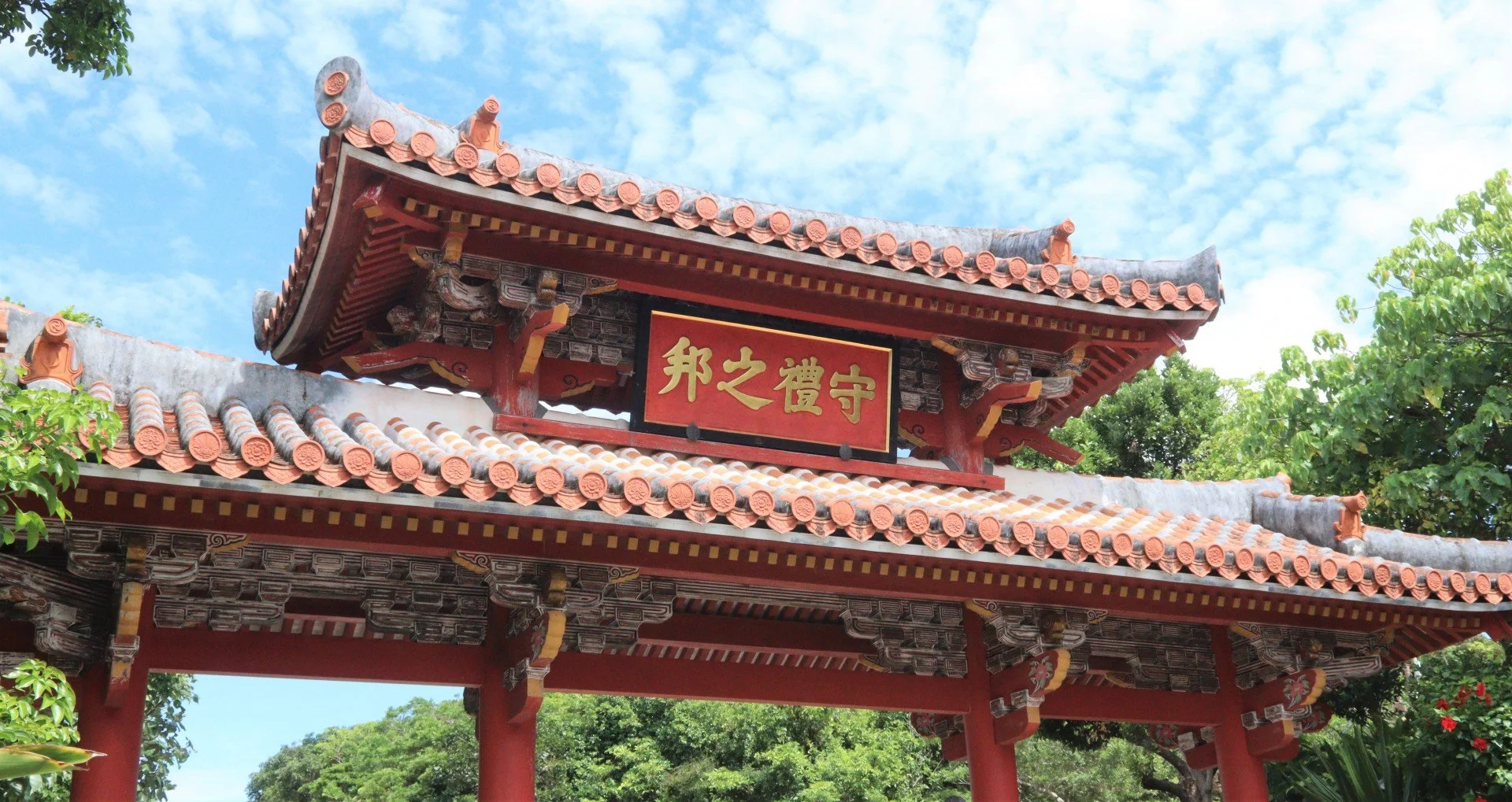 The vermillion Shureimon gate of Shurijo Castle rising against a blue Okinawan sky — a UNESCO World Heritage icon and symbol of Ryukyuan heritage.