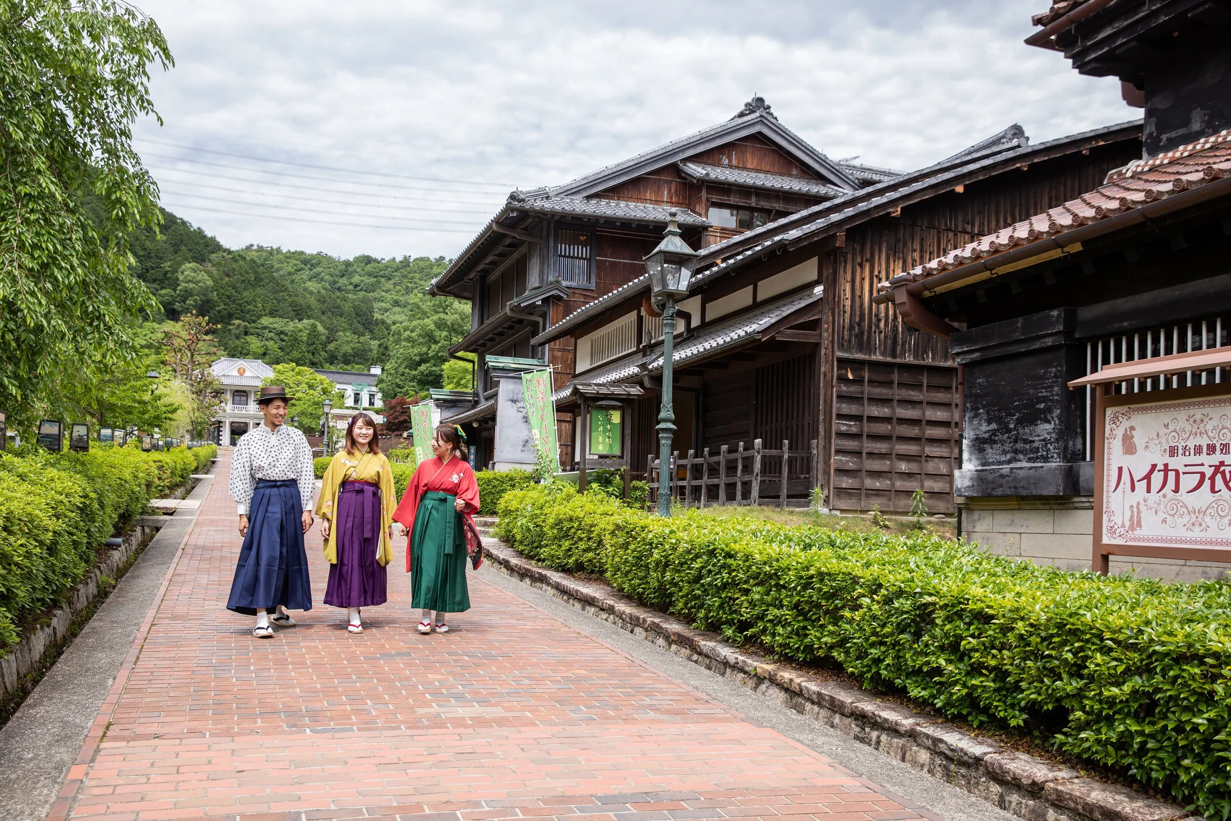 Visitors in colorful hakama strolling a brick path past Meiji-era wooden buildings at Museum Meiji-Mura, Inuyama.