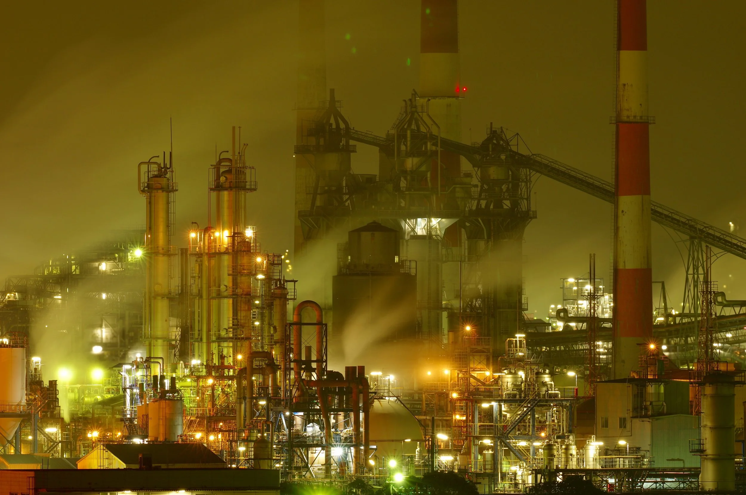 Hundreds of golden lights illuminate Shunan's vast petrochemical complex at night, steam drifting through a sci-fi industrial nightscape on the Seto Inland Sea.