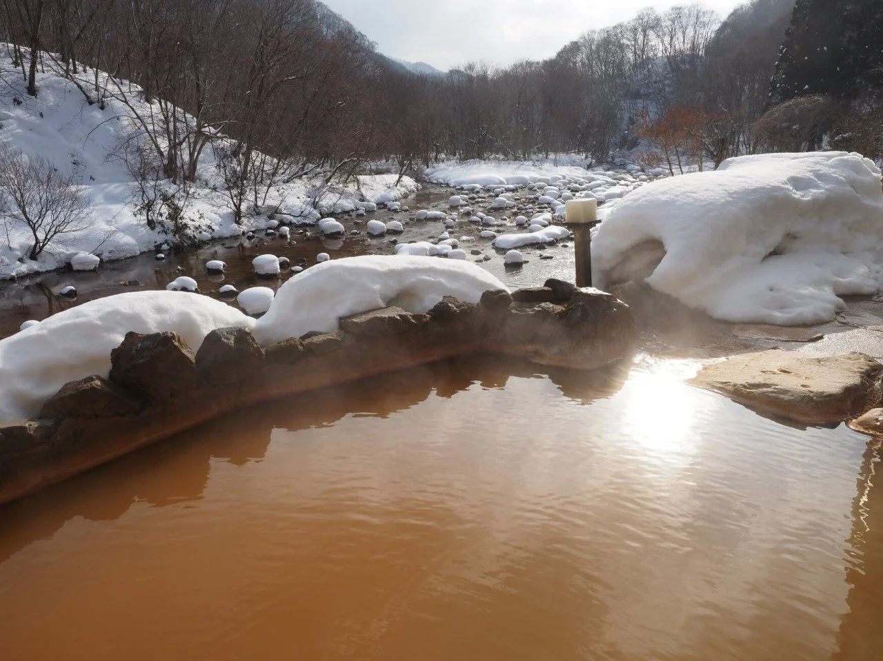 Reddish-brown iron-rich open-air bath at Kenichi Onsen, a 150-year-old riverside inn tucked in the forested hills of Yakumo, Hokkaido.