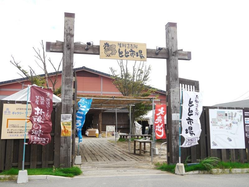 Wooden gate entrance to Toto Ichiba market in Ashiya, Fukuoka, lined with colorful nobori banners — a coastal seafood market and local hidden gem.