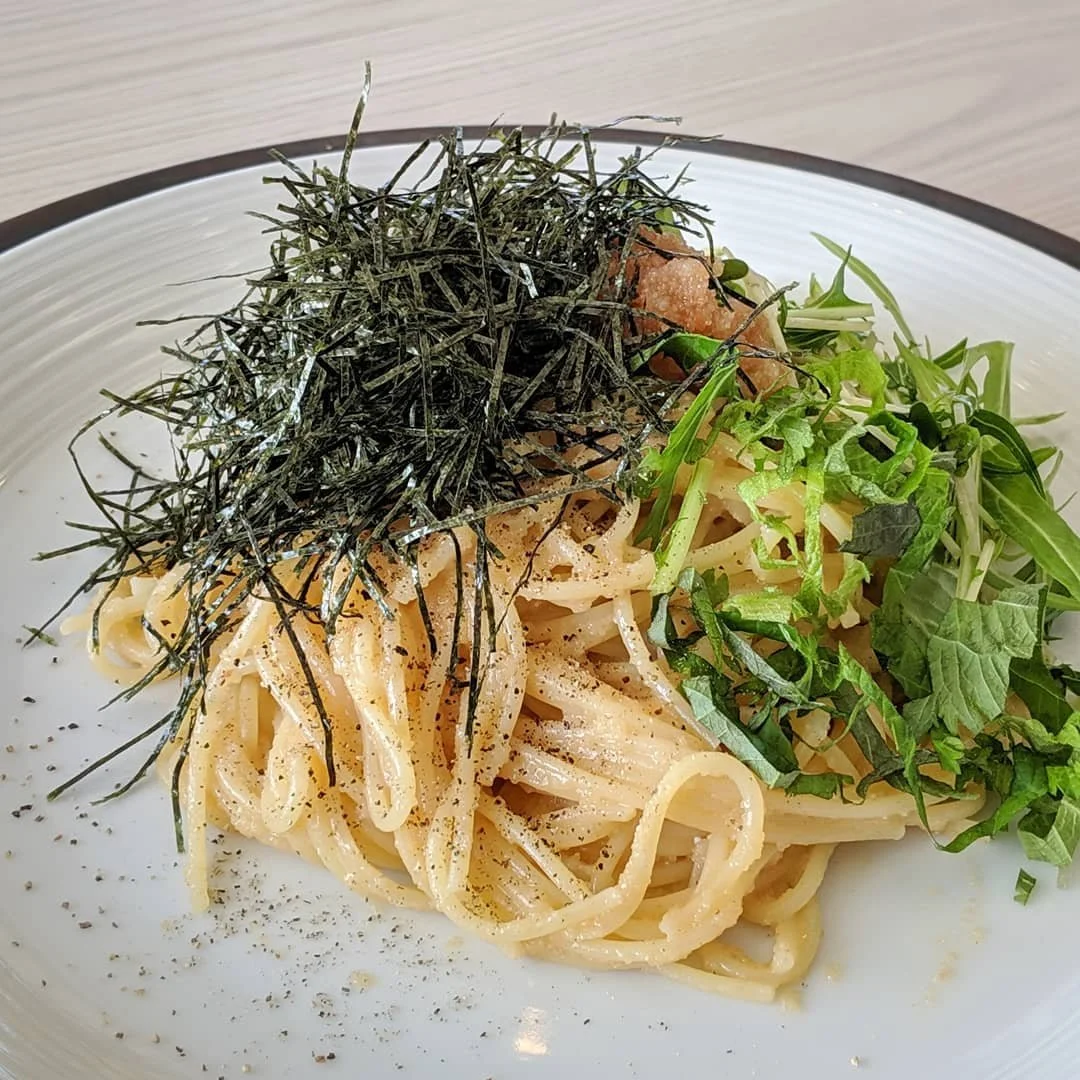 Plate of spaghetti pasta topped with shredded nori, chopped green herbs, and a brown condiment