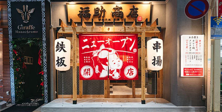 Retro Showa-era storefront of Fukusuke Shoten izakaya in Kokura with red paper lanterns, wooden signboard, and traditional noren curtain at dusk.