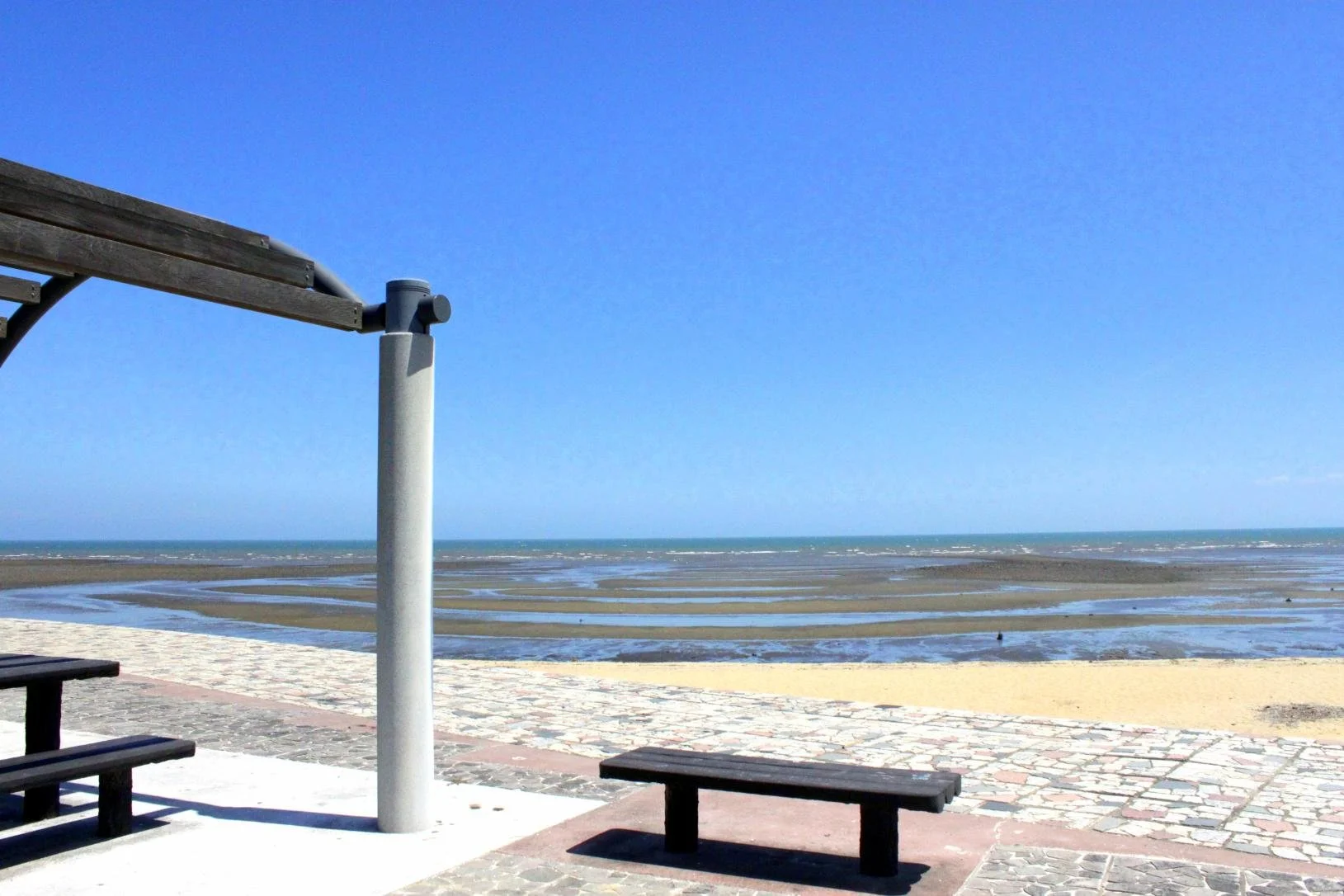 Hamanomiya Beach in Chikujo, Fukuoka — shallow tidal flats stretch under a clear blue sky beside a quiet promenade with wooden benches.