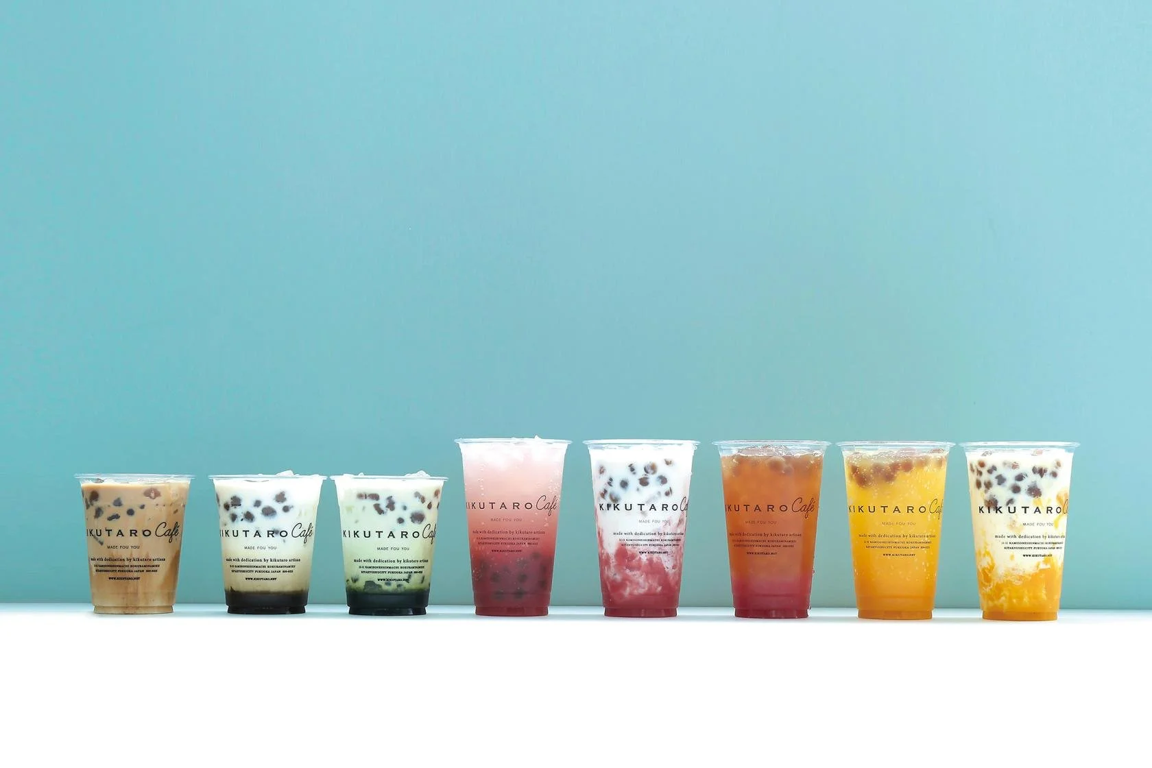 Eight colorful KIKUTARO Café warabi-mochi drinks lined up on a soft teal background — a modern taste of Kitakyushu's traditional sweets.