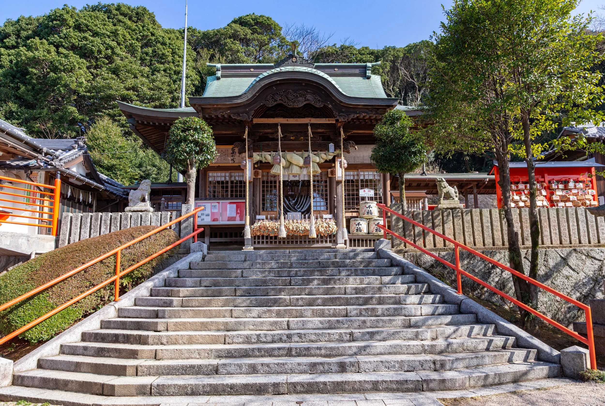 Green-roofed Adachiyama Myoken Shrine at the top of a stone stairway with orange handrails, framed by forest in Kitakyushu, Fukuoka.