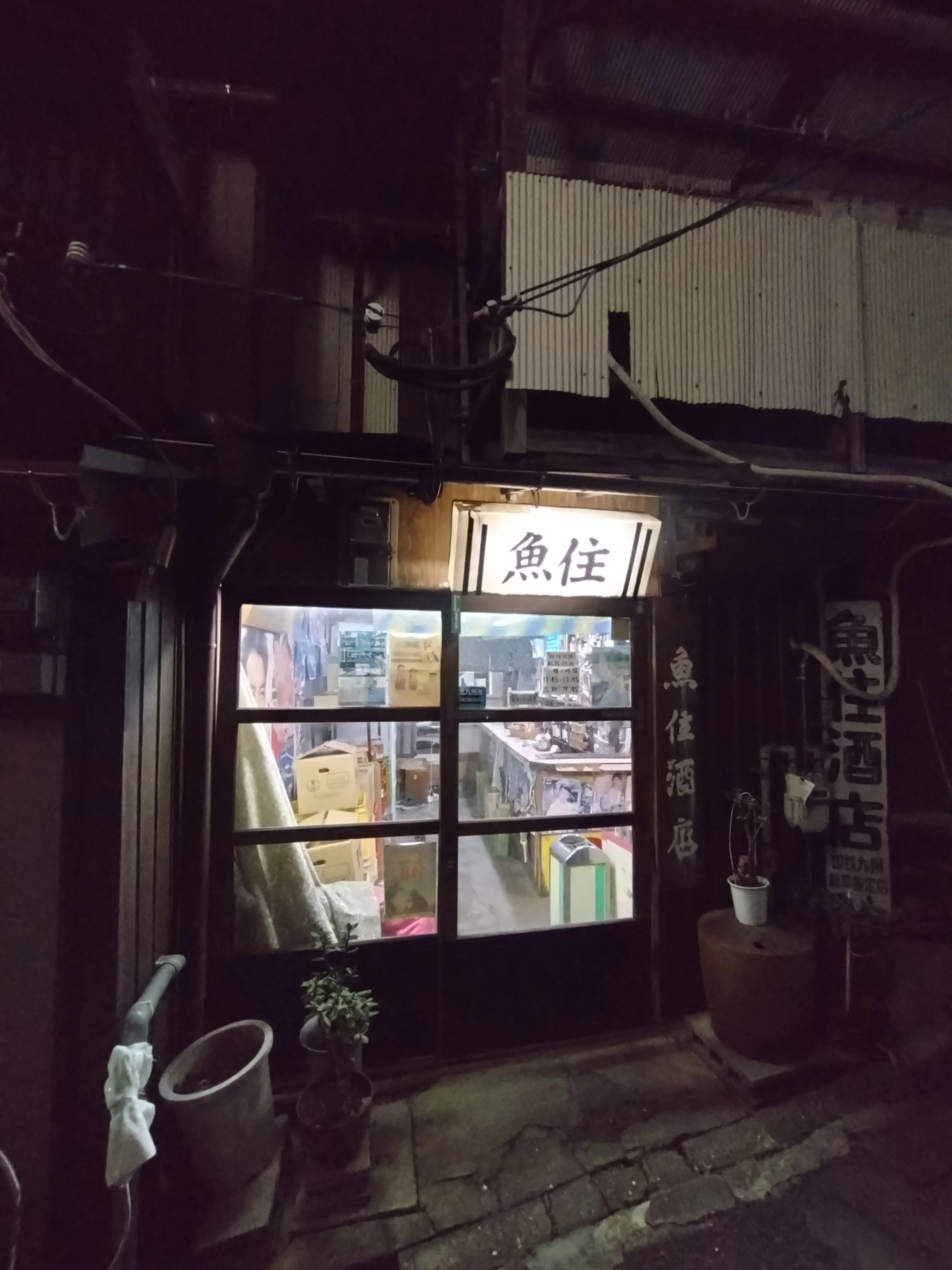 Nighttime storefront of Uozumi Sake Shop in Mojiko, its glowing sign and wooden door welcoming locals to a Showa-era kakuuchi experience.