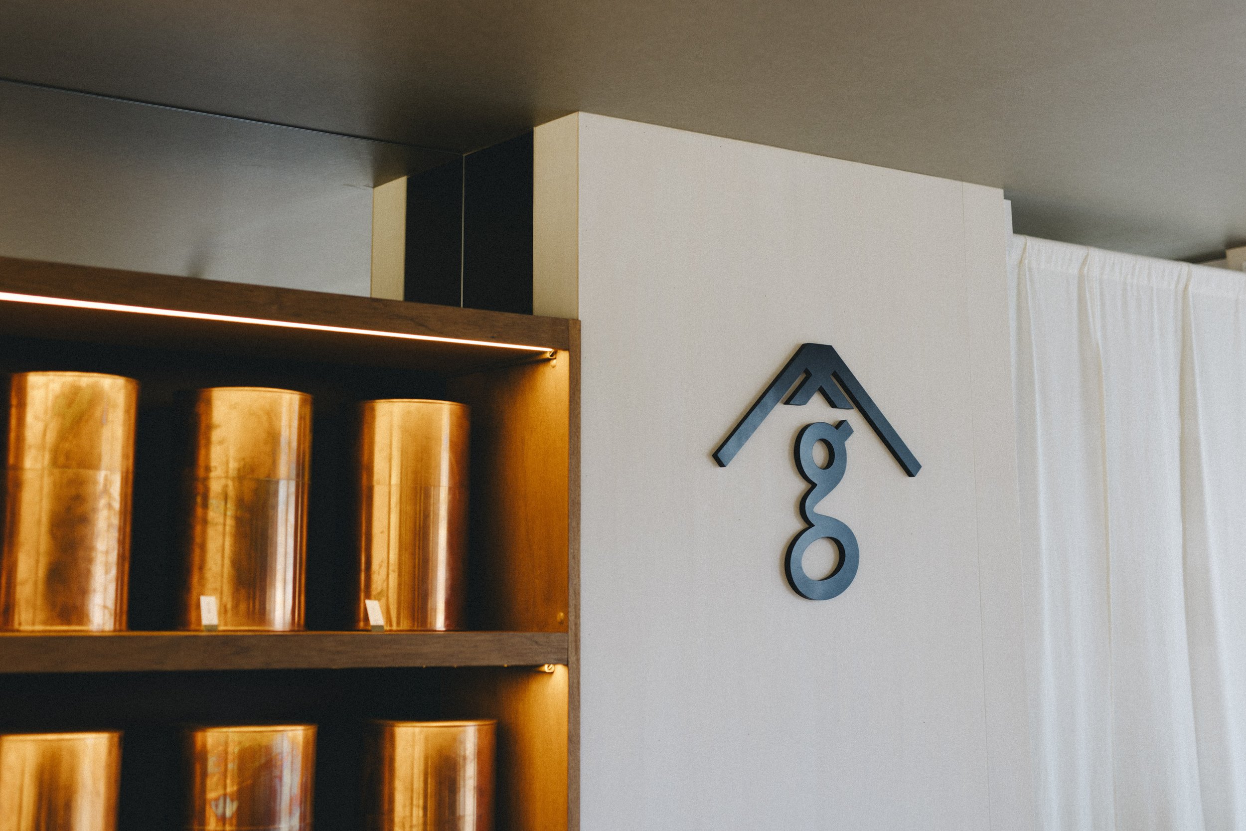 Warm-lit wooden shelves holding copper tea canisters at Sangrams Kikugawa — a 120-year heritage tea shop in Shizuoka, Japan.