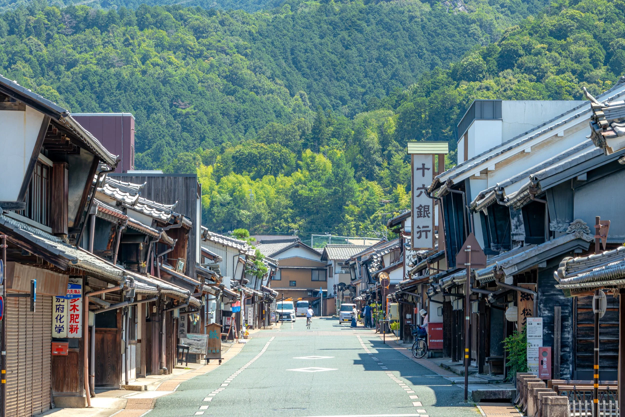 Traditional Edo-period merchant street in Mino, Gifu — udatsu firebreak walls and tiled rooftops leading toward forested hills.