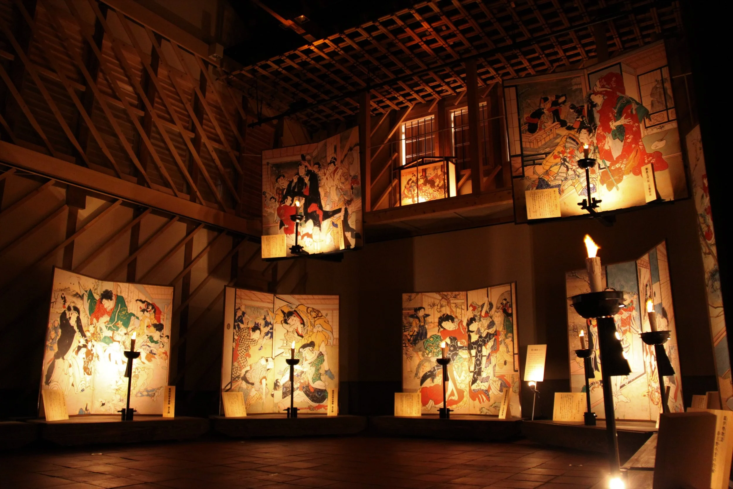 Candlelit exhibition room at Ekingura in Kōchi, glowing folding screens of late-Edo painter Ekin illuminated by flame under wooden rafters.