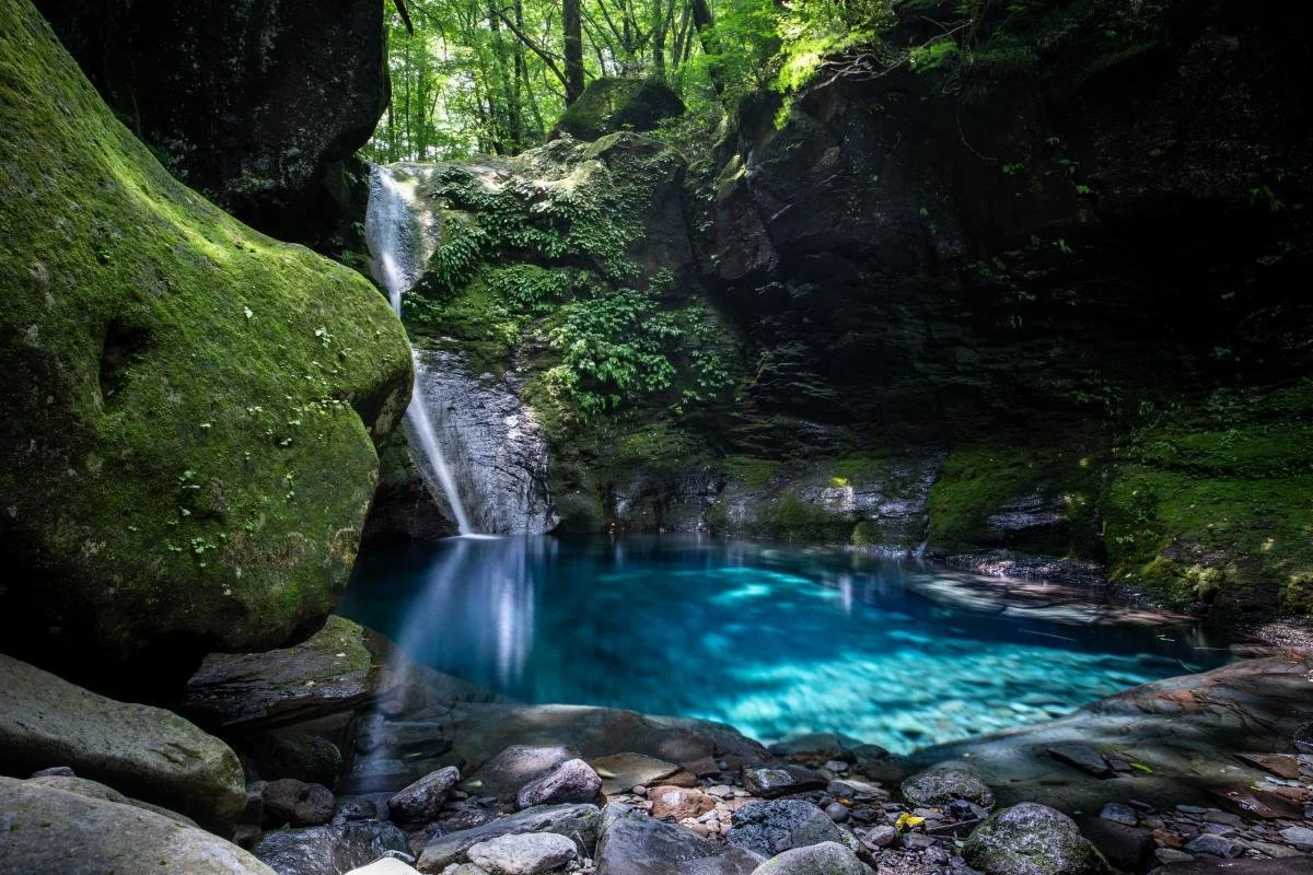 Mystical turquoise-blue pool of Oshiraji Falls framed by moss-covered boulders and forest in Yaita, Tochigi — a hidden phantom waterfall in Japan.