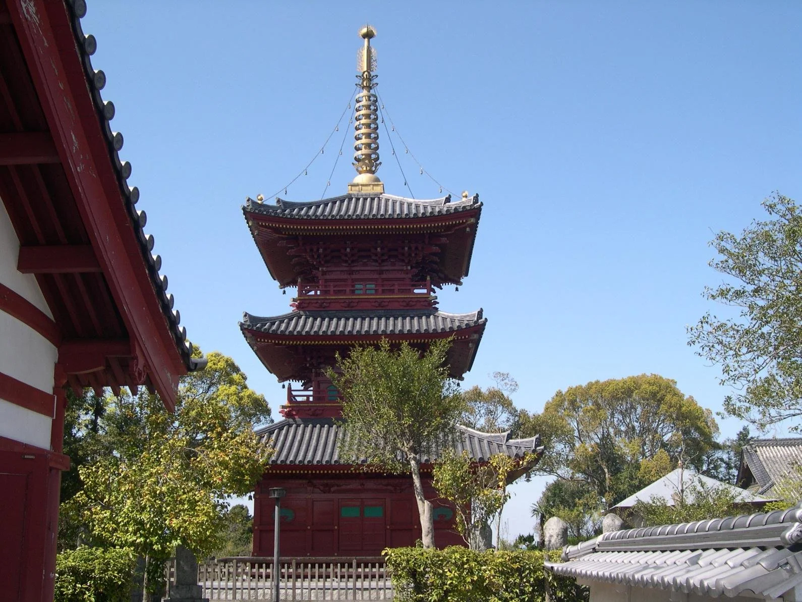 Vermilion three-story pagoda rising against a clear blue sky at the historic Buzen Kokubunji Temple Site in Miyako Town, Fukuoka.