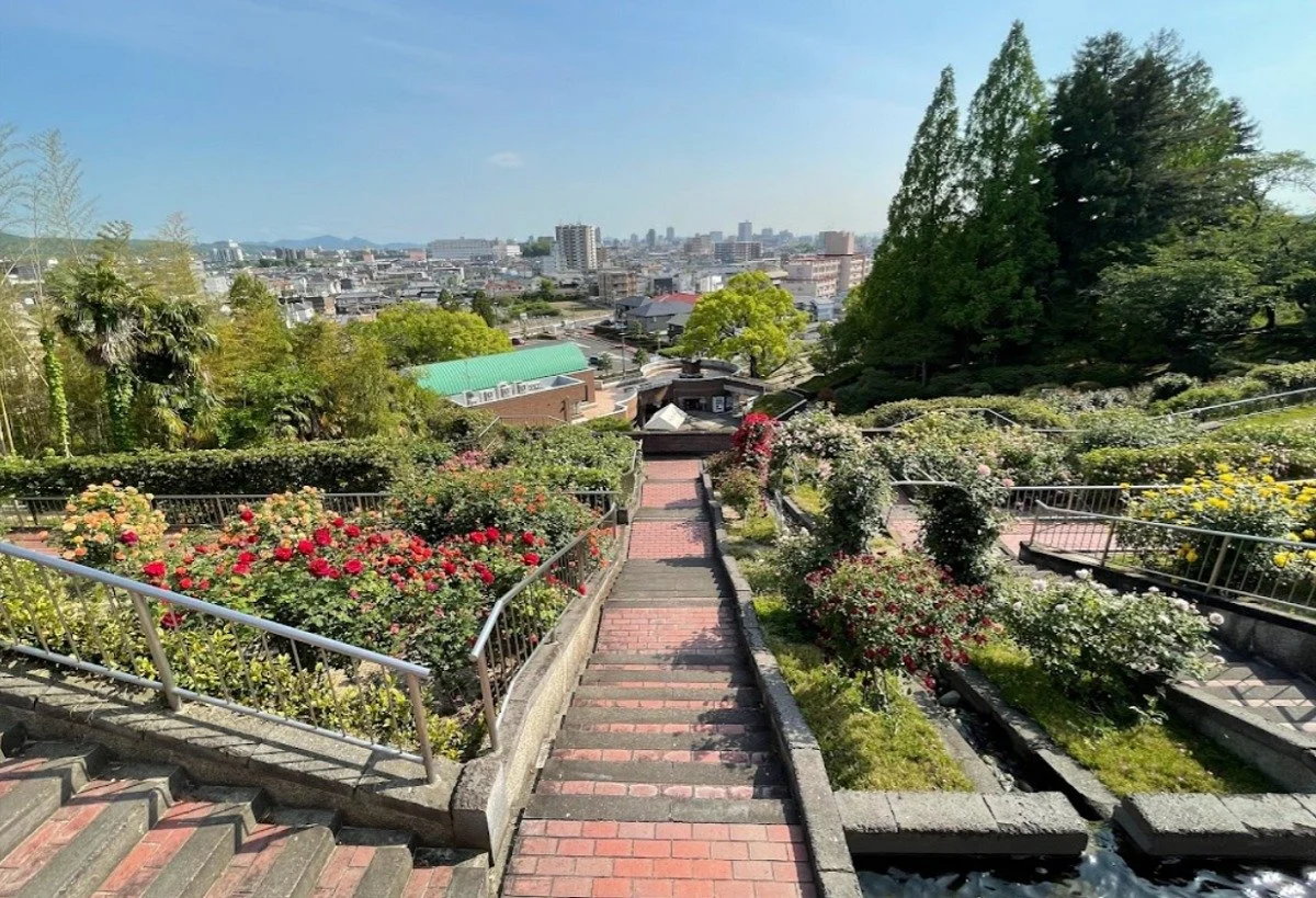 Terraced flower beds and a brick staircase at Handayama Botanical Garden overlooking Okayama City under a clear blue sky.