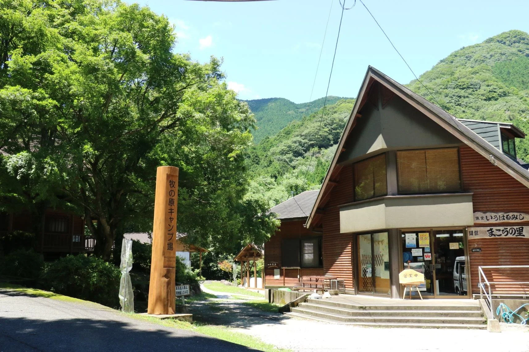Wooden lodge and signpost of Makinoharu Campground on a lush green plateau in Chikujyo Town, Fukuoka—a forest-bathing retreat away from the city.