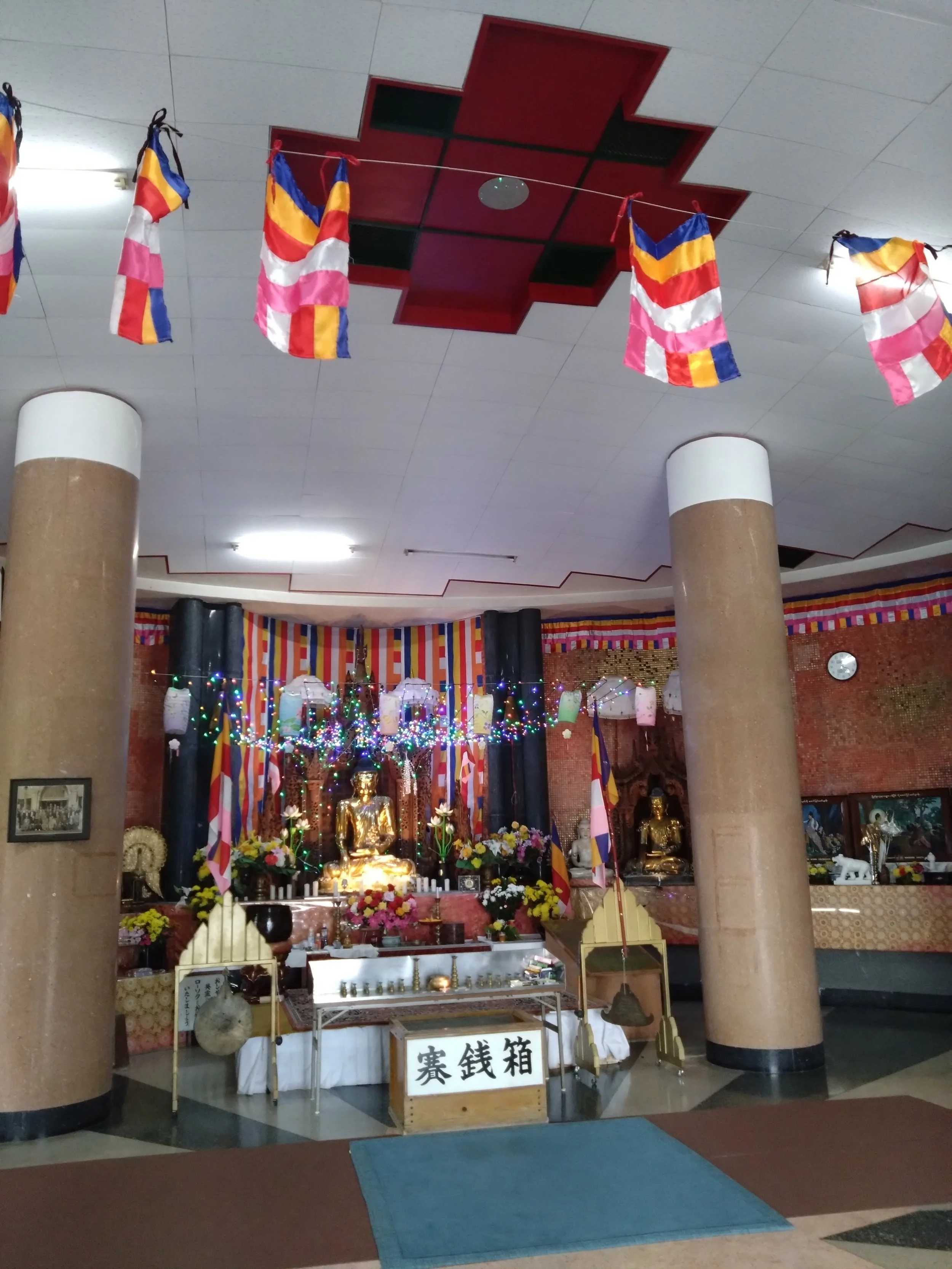Vibrant Buddhist altar with golden statues and colorful prayer flags inside Japan's only Burmese-style temple, the World Peace Pagoda in Mojiko.