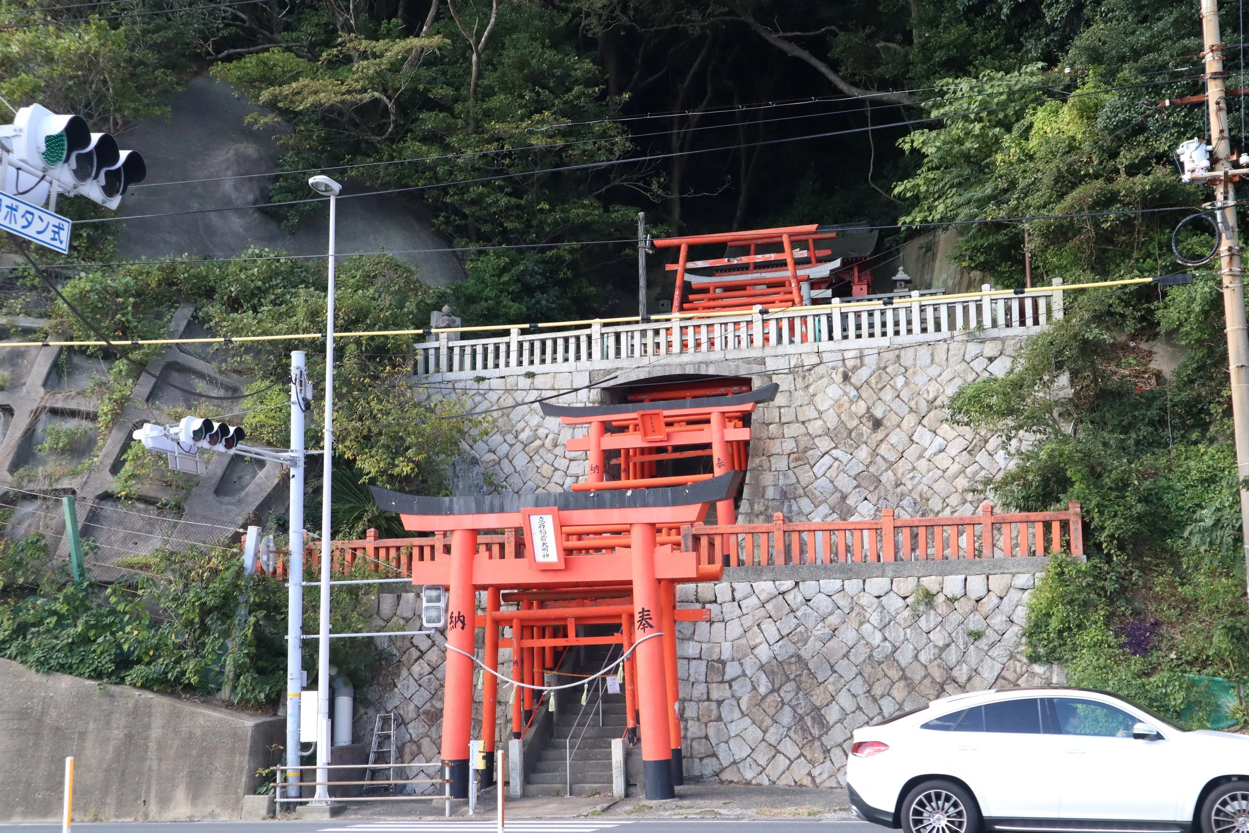 Red torii gates ascending a stone retaining wall at Tateishi Inari Daimyojin, a seaside shrine tucked into a quiet Shimonoseki street.