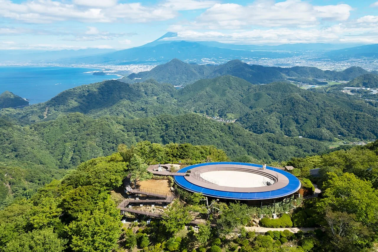 Aerial view of Izu Panorama Park's sky garden atop Mount Katsuragi, with Mount Fuji and Suruga Bay stretching to the horizon.