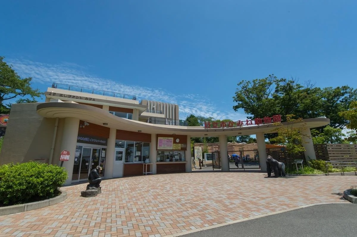 Sunlit entrance plaza of Hitachi City Kamine Zoo in Ibaraki, with gorilla and primate statues greeting visitors beneath a bright blue sky.